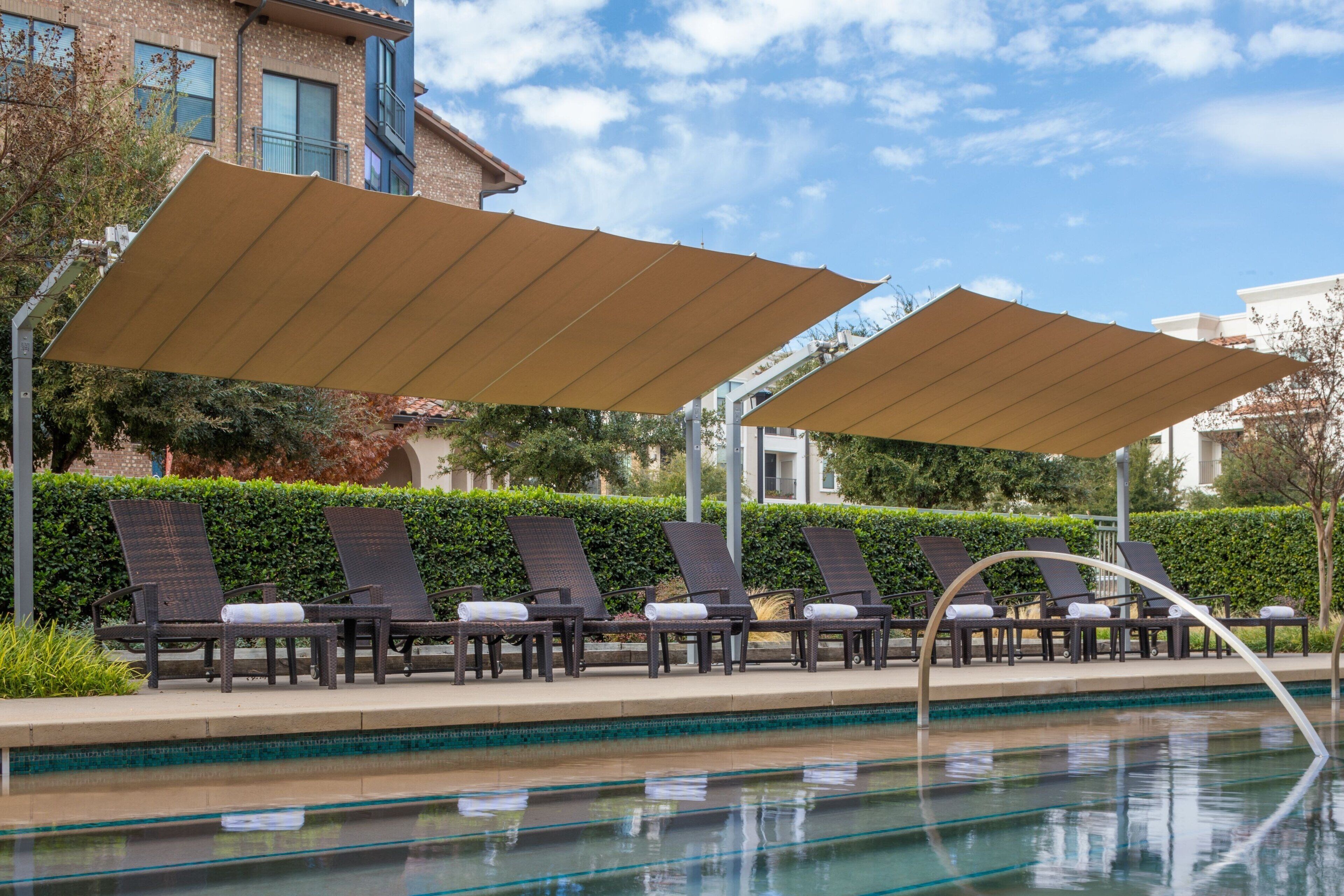 Area piscina con poltronne a sdraio e ombrelloni, una piscina limpida e un edificio sullo sfondo.
