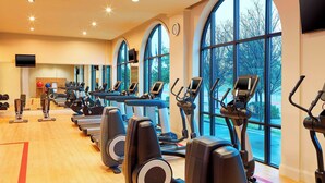 A gym with multiple treadmills and elliptical machines, large windows, and a clock on the wall. - Sheraton Stonebriar Hotel (Frisco)