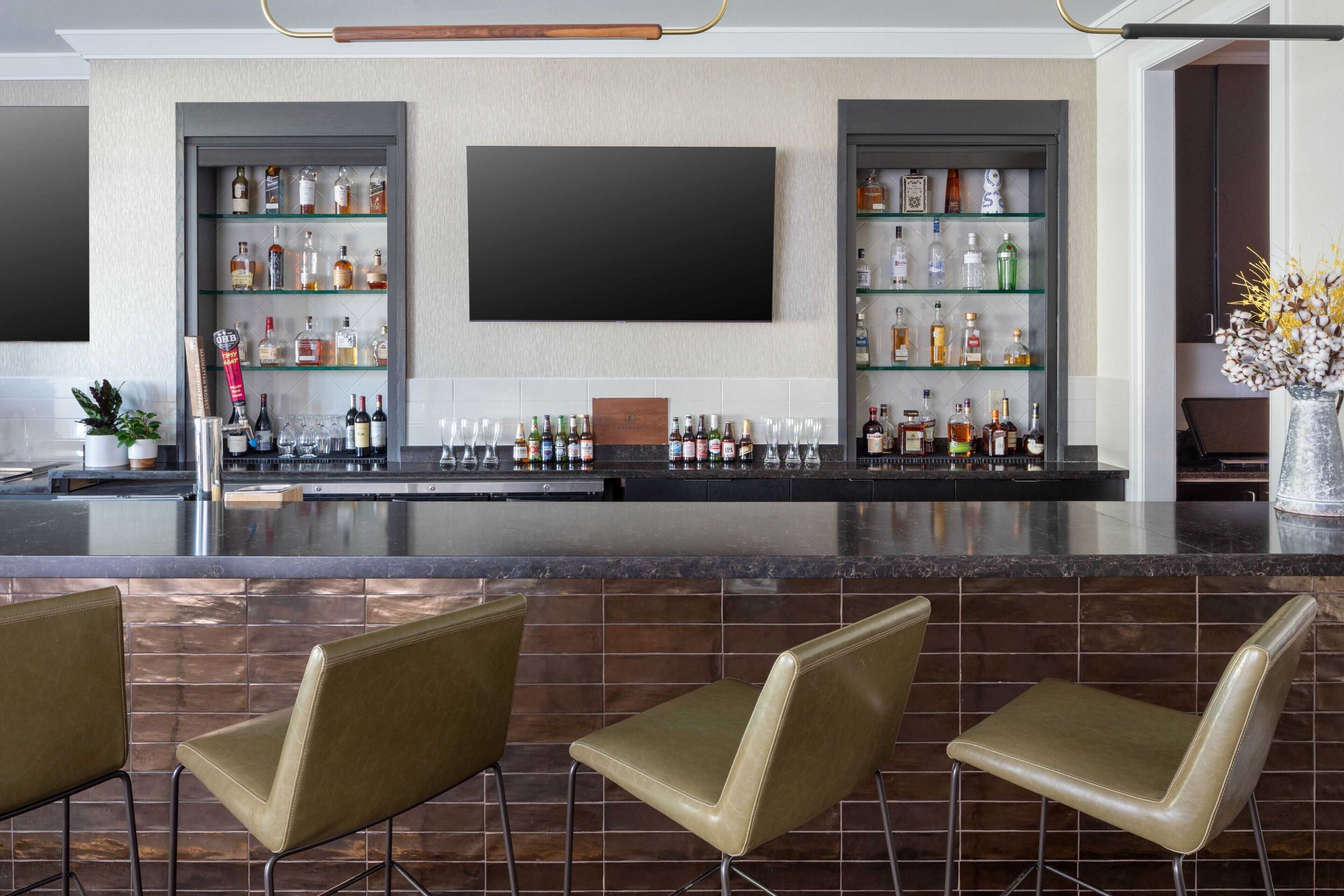 Een bar met een flatscreen televisie, planken vol drankflessen en drie barkrukken.
