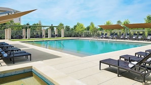 A rectangular swimming pool with lounge chairs and umbrellas around it, set against a backdrop of trees and a clear sky. - Sheraton Stonebriar Hotel (Frisco)