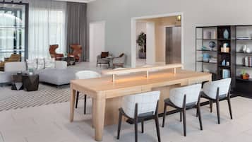 A modern living room with a wooden dining table, white chairs, a grey sofa, and a black bookshelf.