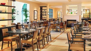 A spacious dining area with multiple tables and chairs, a fireplace, and shelves with decorative items. - Sheraton Stonebriar Hotel (Frisco)