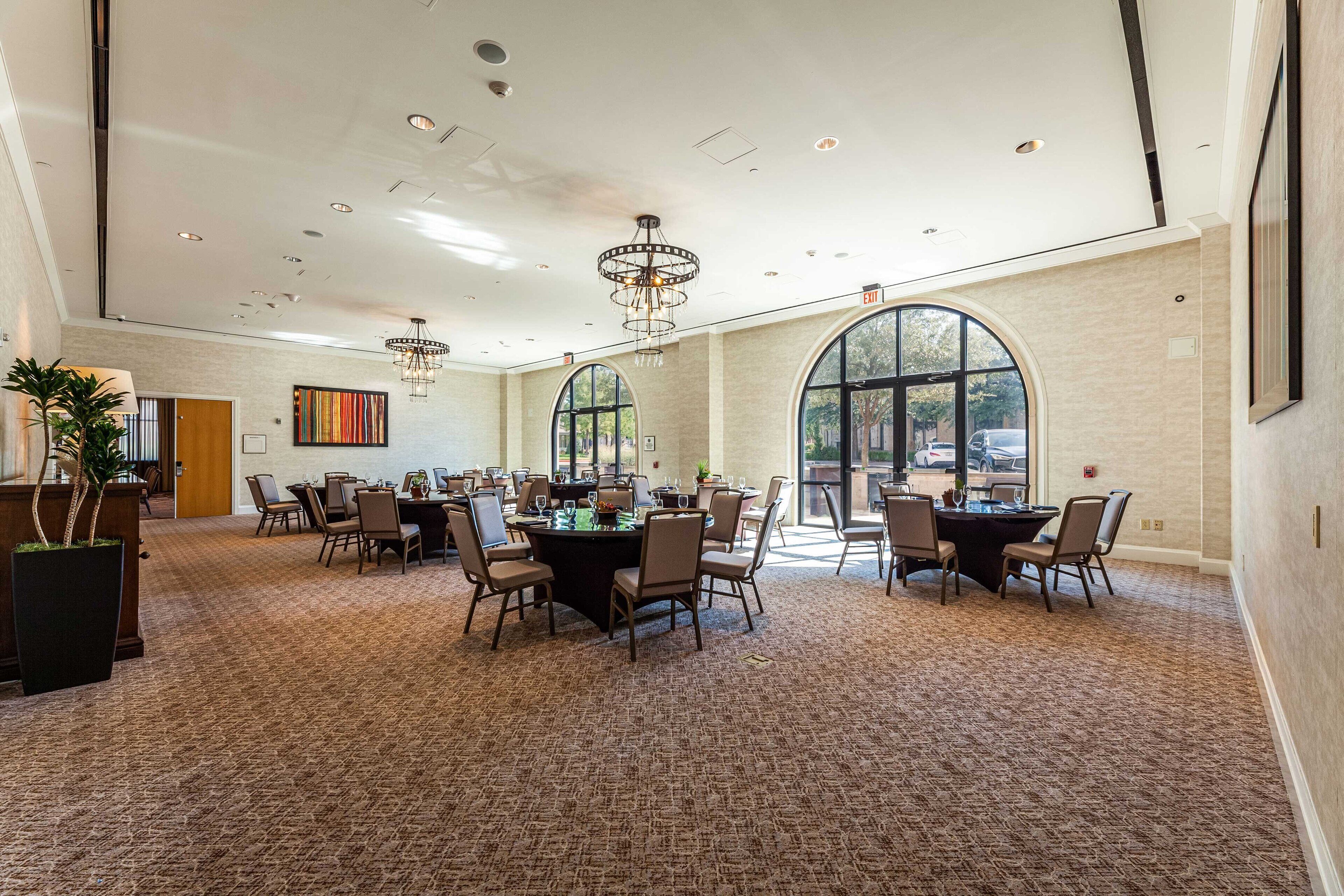 A spacious conference room with multiple tables and chairs, large windows, and modern lighting fixtures.