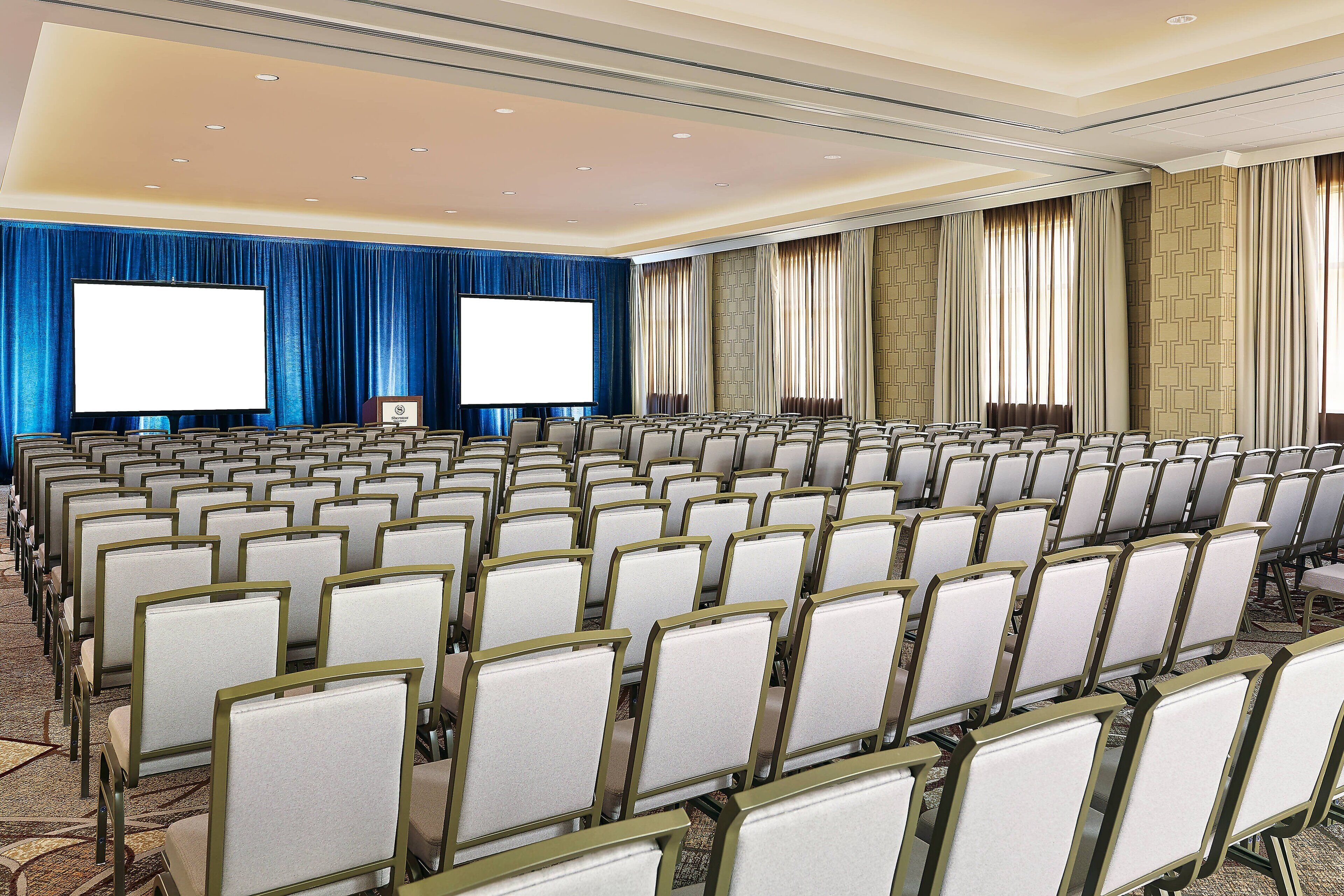 A conference room with rows of chairs, a large screen, and curtains.