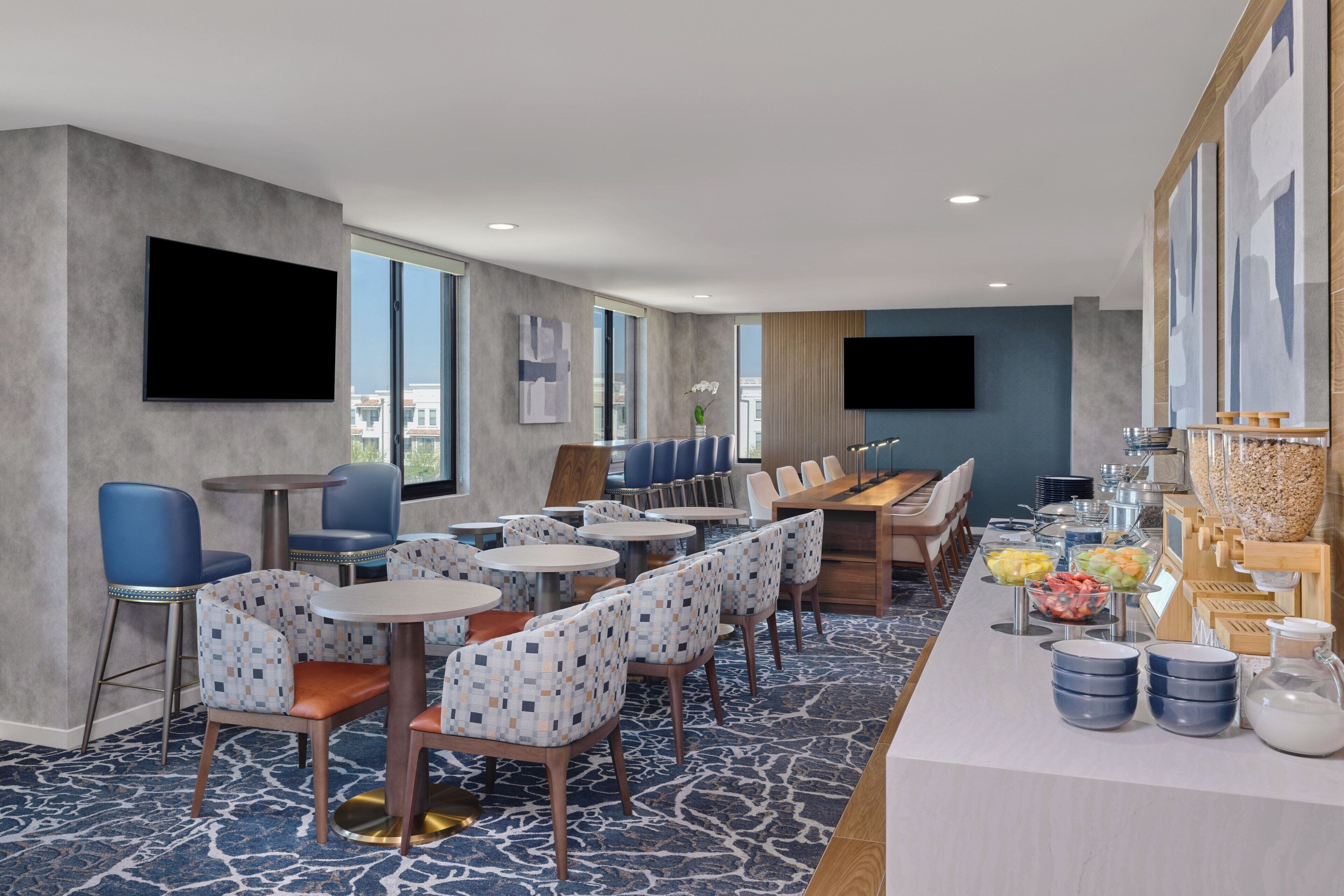 A hotel dining area with round tables, blue chairs, and a buffet with various food items.