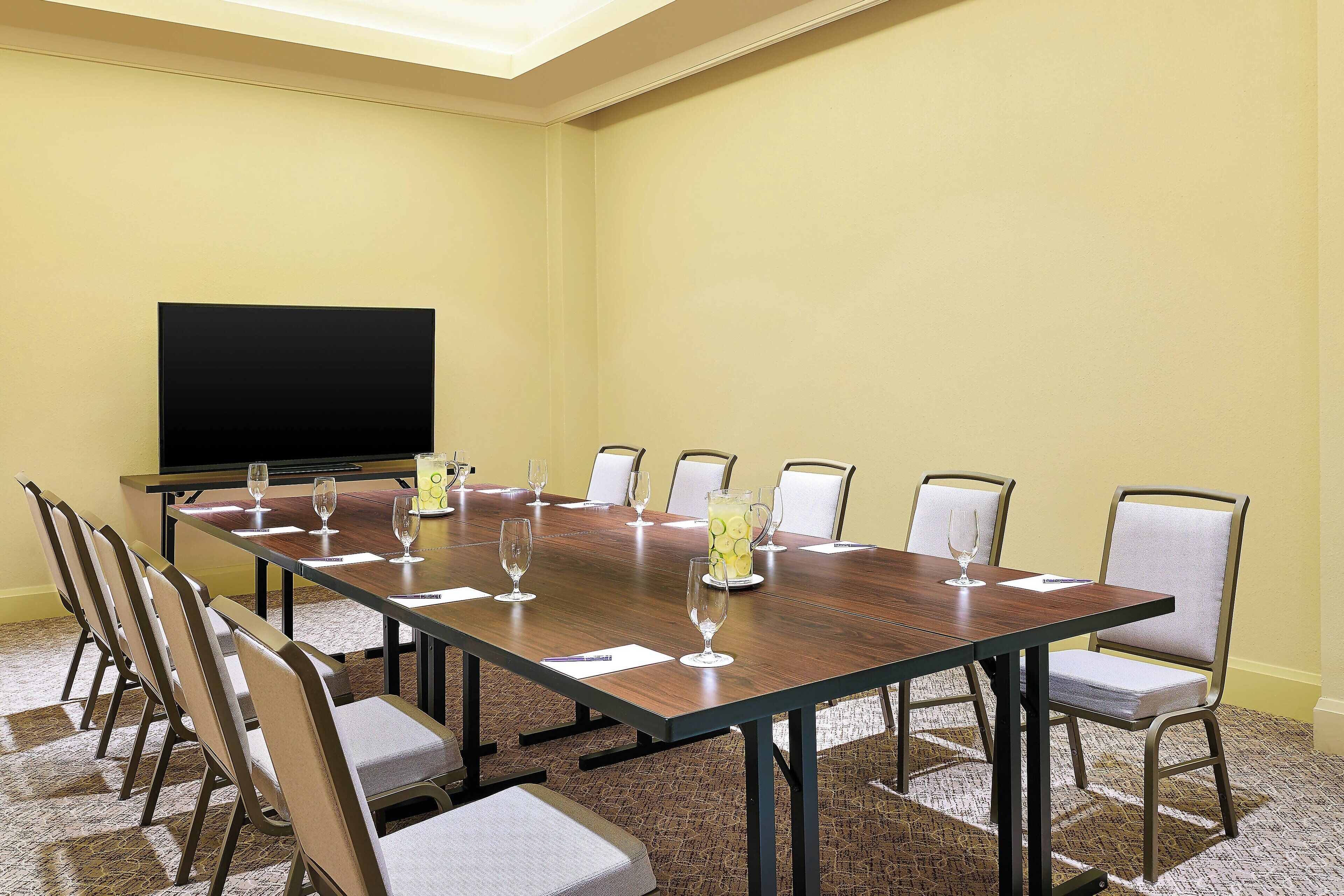 A conference room with a long table, chairs, a projector screen, and a pitcher of water.