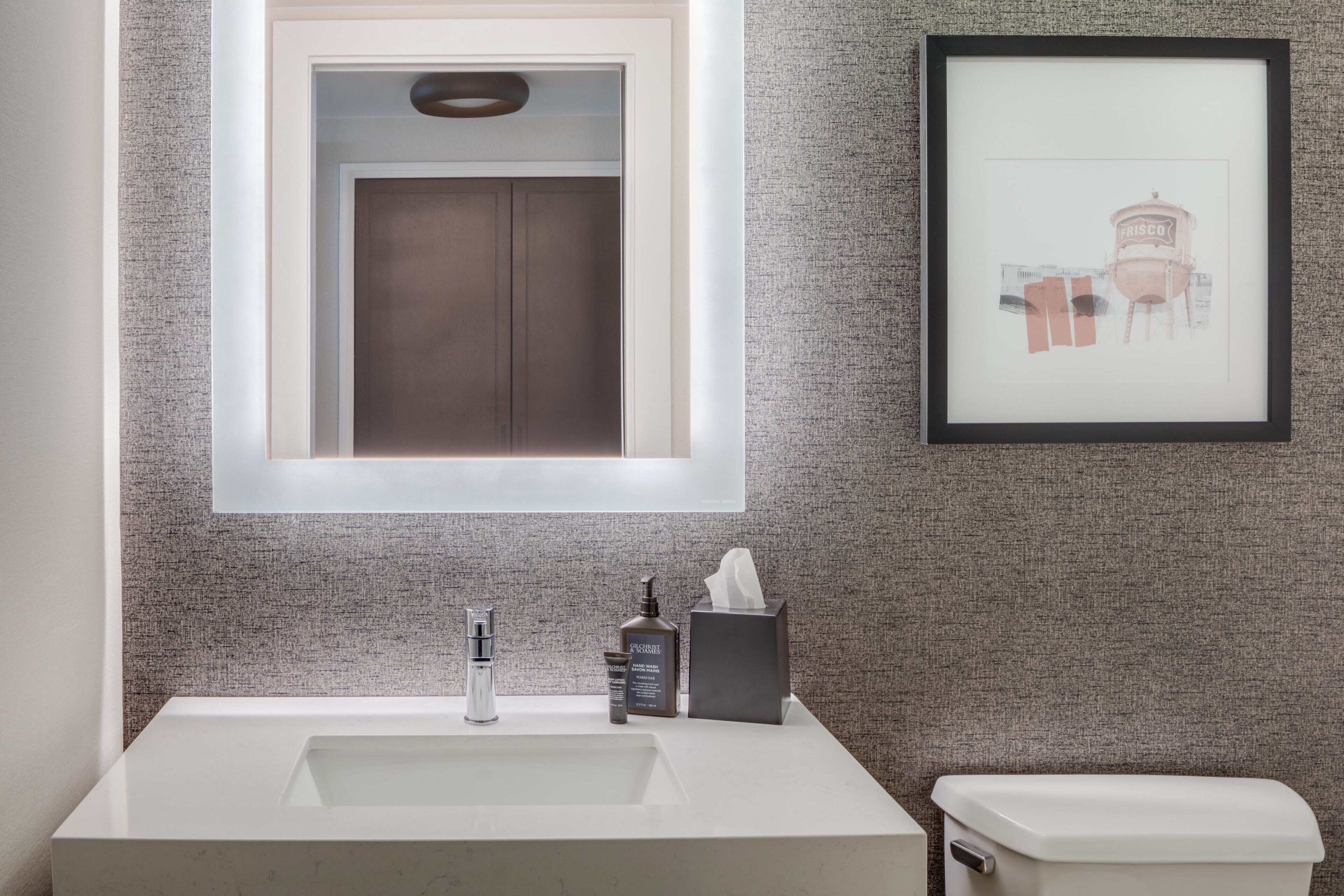 A bathroom with a large mirror, a sink, a toilet, and a framed picture on the wall.