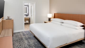Habitación de hotel con una cama grande, una mesita de noche con lámpara, cabecero de madera, televisor sobre un mueble bajo y alfombra estampada.