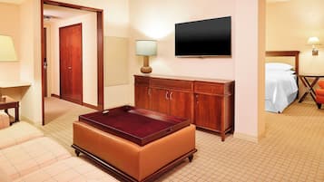 Una habitación de hotel con sofá, una mesita, un armario, televisión y cama.
