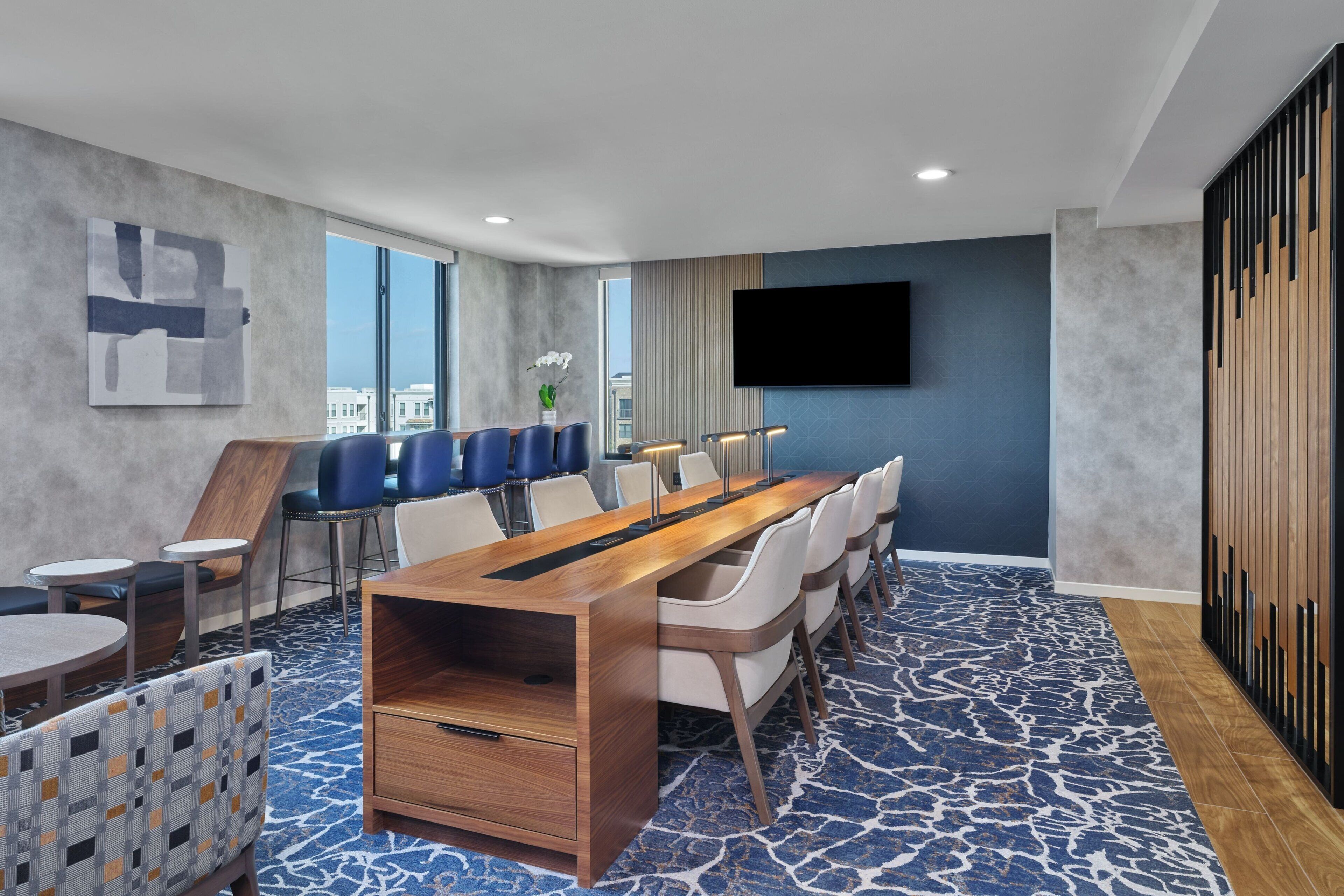 A modern conference room with a long table, chairs, and a large screen.