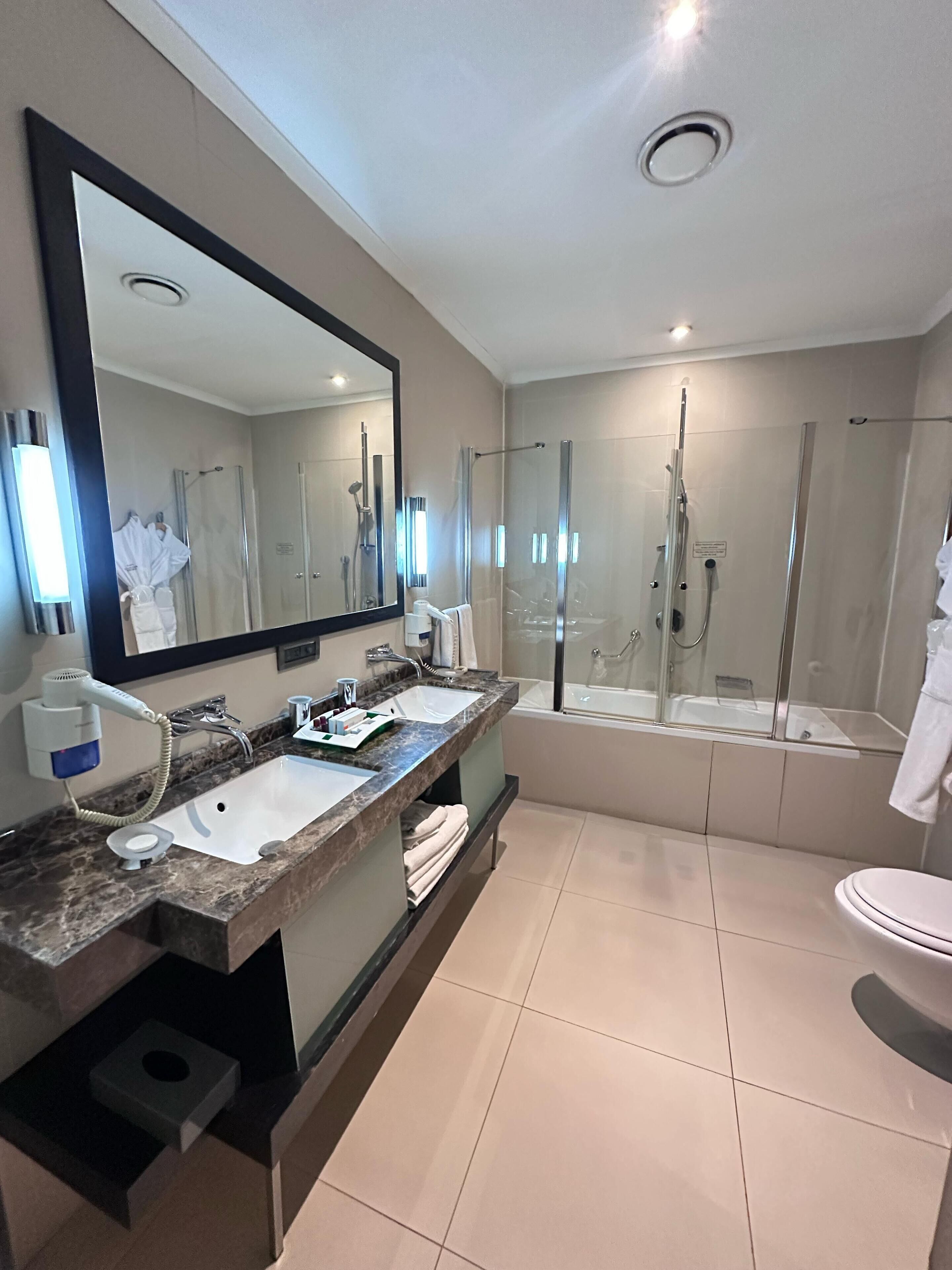 A modern bathroom with dual sinks, a large mirror, a shower enclosure, and a toilet.