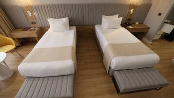 A hotel room with two beds, a wooden nightstand, a desk, a chair, and a lamp.