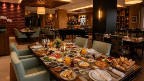 A dining area with a long table set for a meal, surrounded by chairs, with a bar and piano in the background. - ADM Grand Hotel (Istanbul)