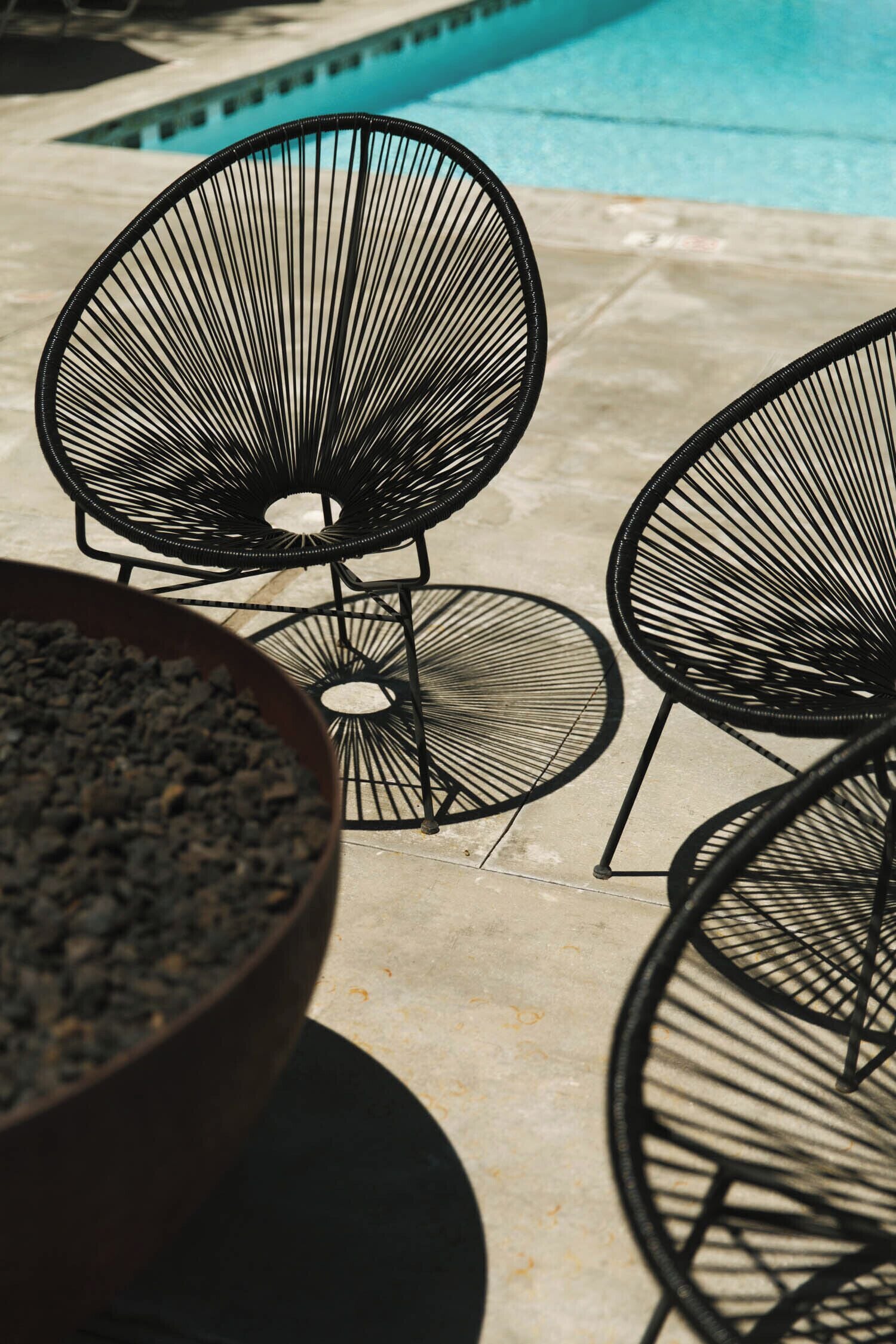 Outdoor seating with metal chairs and a large bowl of charcoal.