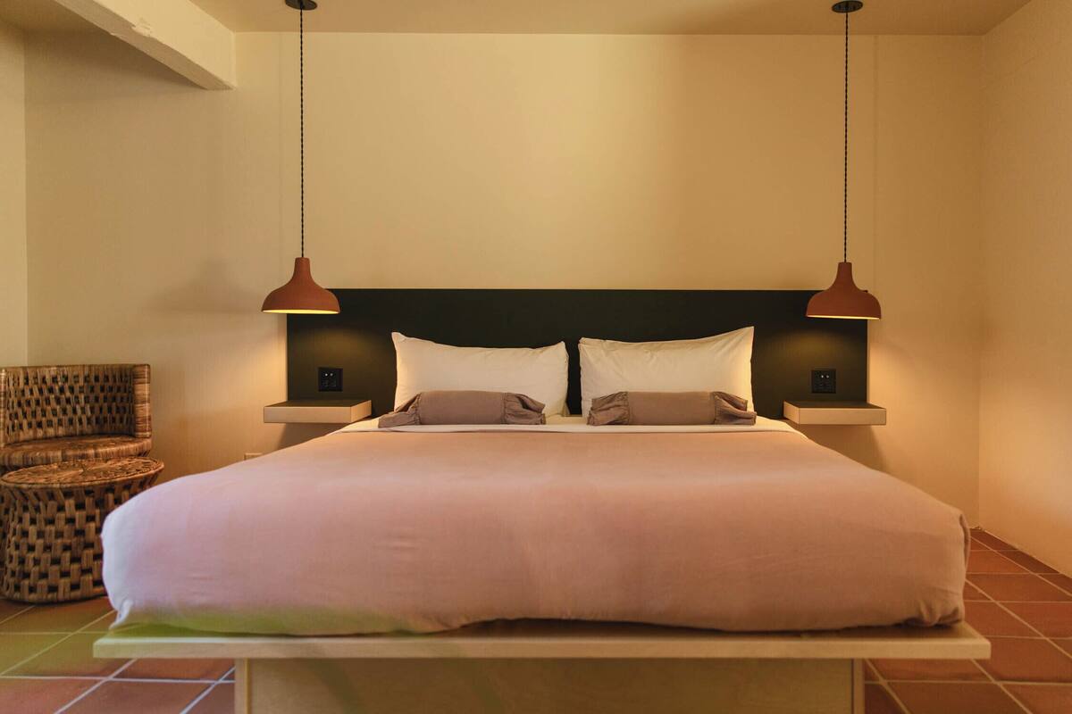 A neatly made bed with a headboard, two bedside lamps, and a woven chair.
