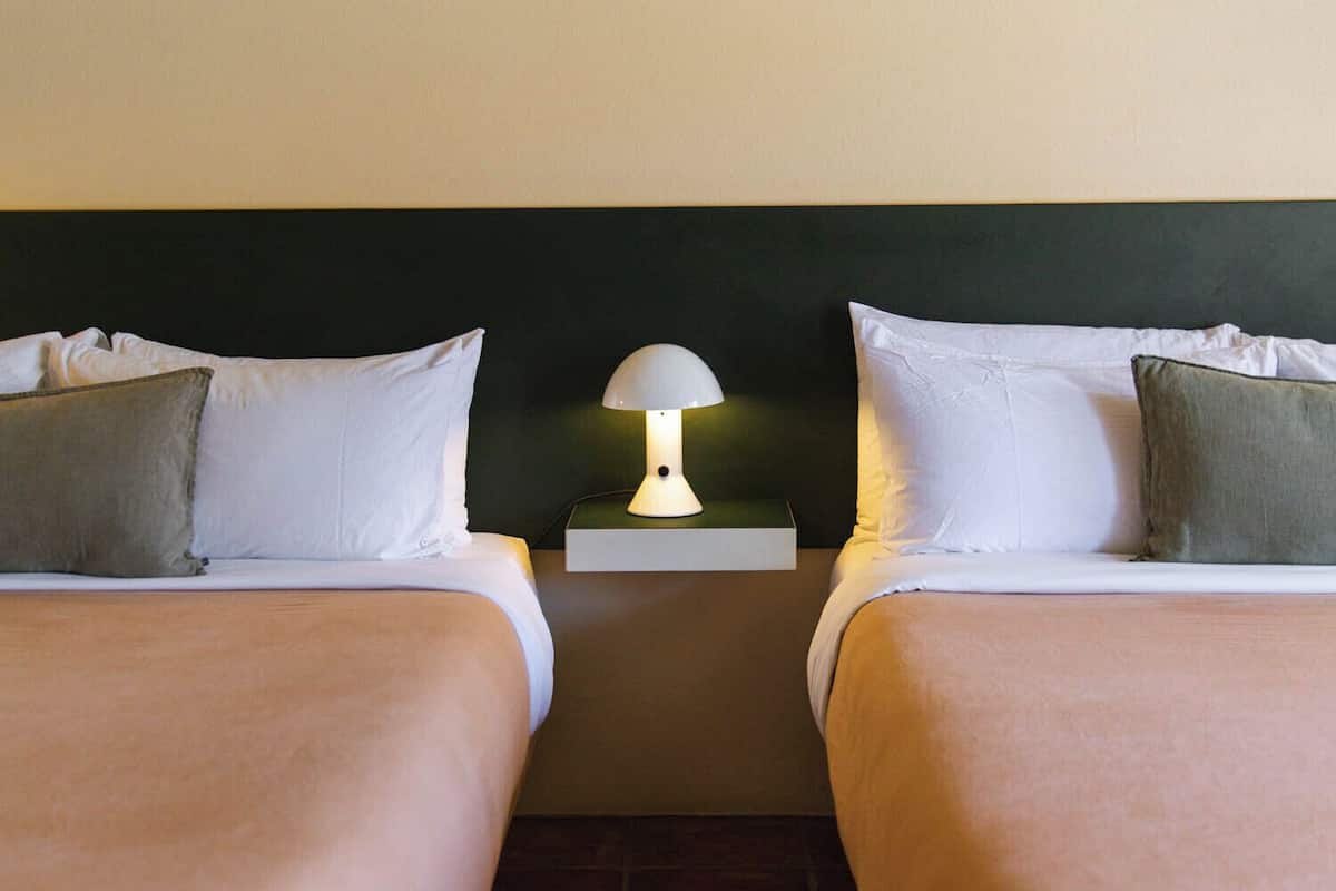 A twin room with two beds, a nightstand with a lamp, and a tiled floor.