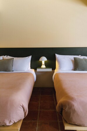 A twin room with two beds, a nightstand with a lamp, and a tiled floor.