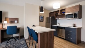 A modern kitchen with a central island, stainless steel appliances, and blue chairs. - Candlewood Suites Lake Charles - Sulphur by IHG (Sulphur)
