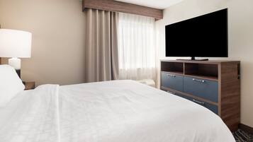 Habitación de hotel con una cama grande, un televisor de pantalla plana, un escritorio con lámpara, un armario y una ventana con cortinas.