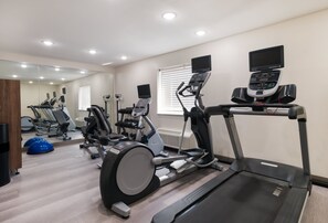 A modern gym with various cardio machines, including treadmills and stationary bikes, and a mirrored wall.
