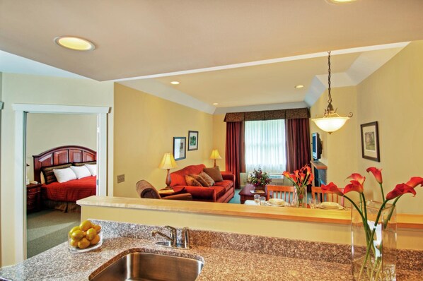 Habitación de hotel con área de cocina, una mesa de comedor, un sofá rojo y una cama con cabecera roja.