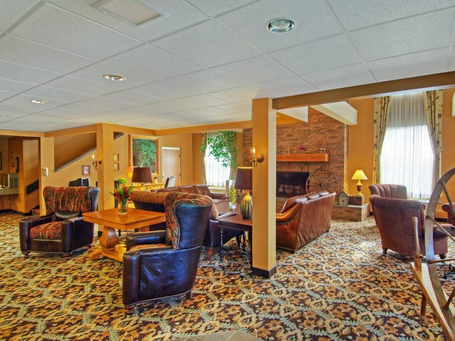 Un hall de hotel espacioso con alfombra estampada, asientos de cuero, chimenea y un ventanal con cortinas.