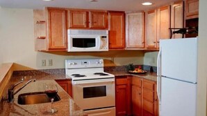 A kitchen with wooden cabinets, a white microwave, a stove, and a refrigerator. - Pointe at Castle Hill Resort (Cavendish)