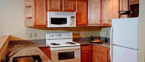 A kitchen with wooden cabinets, a white microwave, a stove, and a refrigerator.
