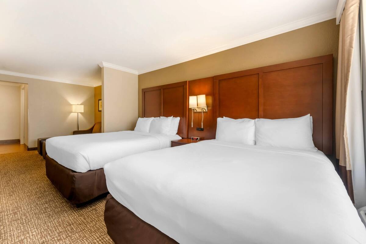 A hotel room with two beds, a wooden headboard, bedside lamps, and a carpeted floor.