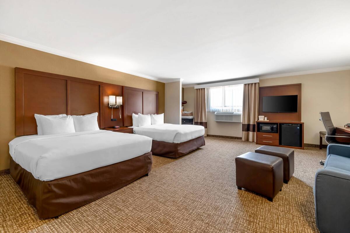A hotel room with two beds, a desk, a TV, and a seating area.