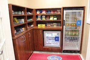 A compact kitchenette with wooden cabinets, a small refrigerator, and a variety of snacks and beverages. - Comfort Suites Elizabethtown (Elizabethtown)