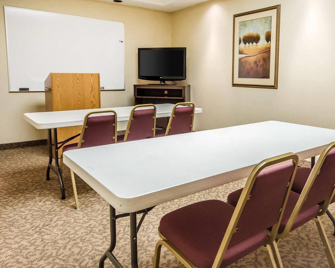 A conference room with a long table, six chairs, a whiteboard, a television, and a painting on the wall.
