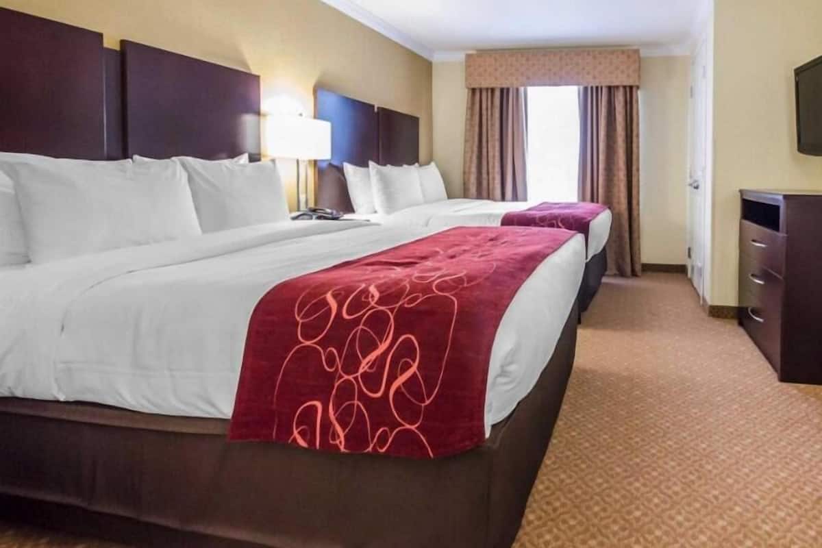 A hotel room with two beds, a desk, a lamp, and a television.