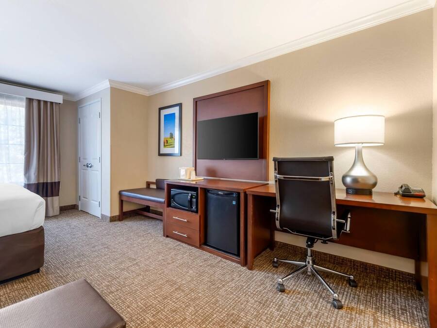 A hotel room with a bed, a desk with a computer, a television, a lamp, and a small refrigerator.