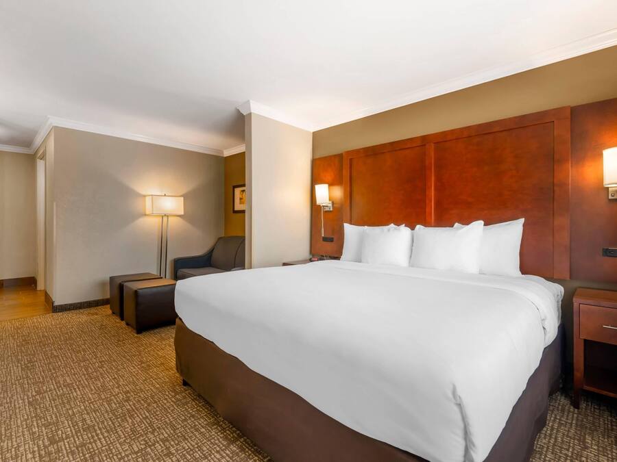 A hotel room with a large bed, two bedside tables, a nightstand, a chair, and a lamp.