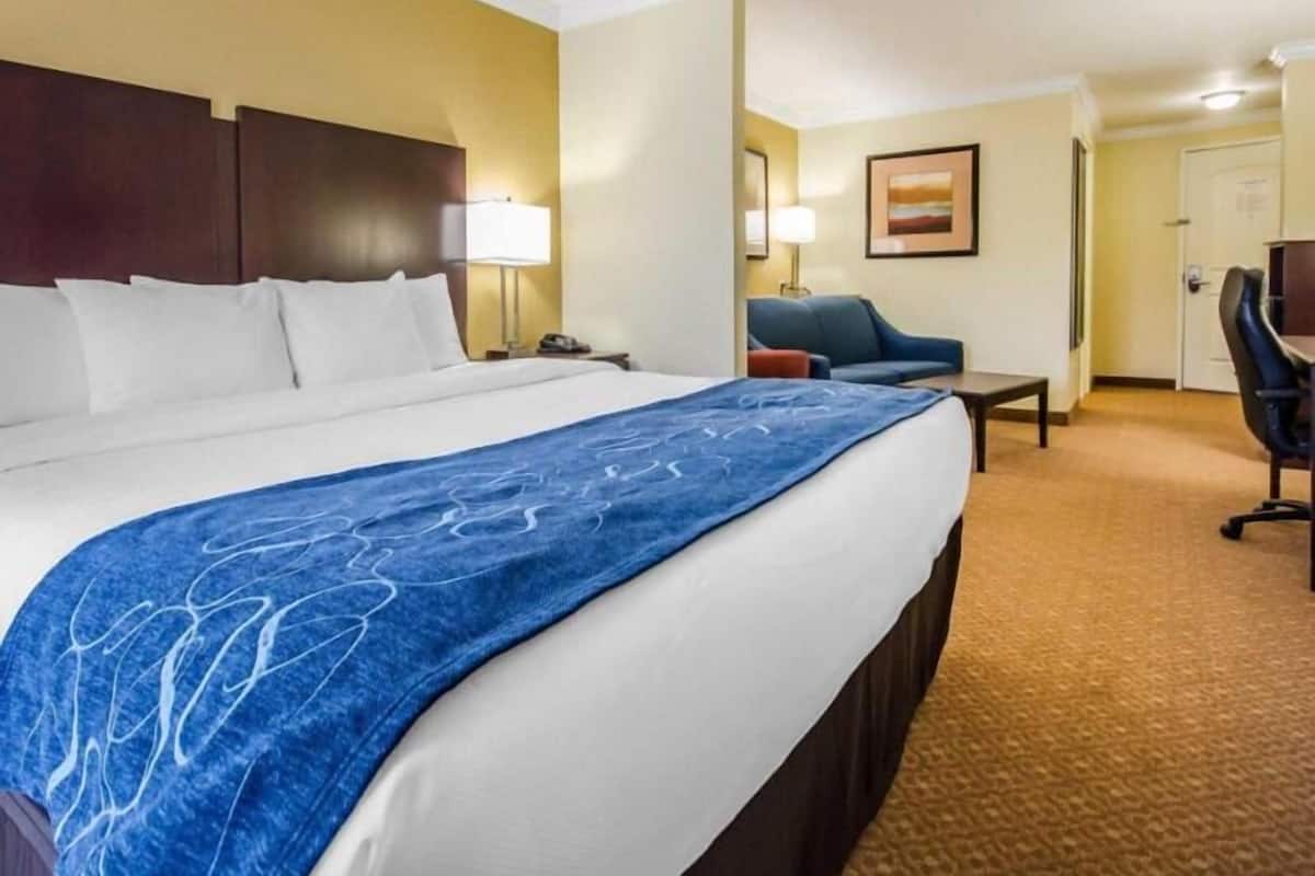 A hotel room with a large bed, a desk, a chair, and a lamp.