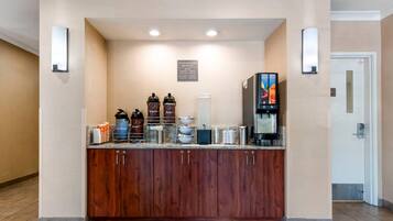 A hotel breakfast area with a wooden counter, coffee machines, and a sign indicating complimentary breakfast hours.