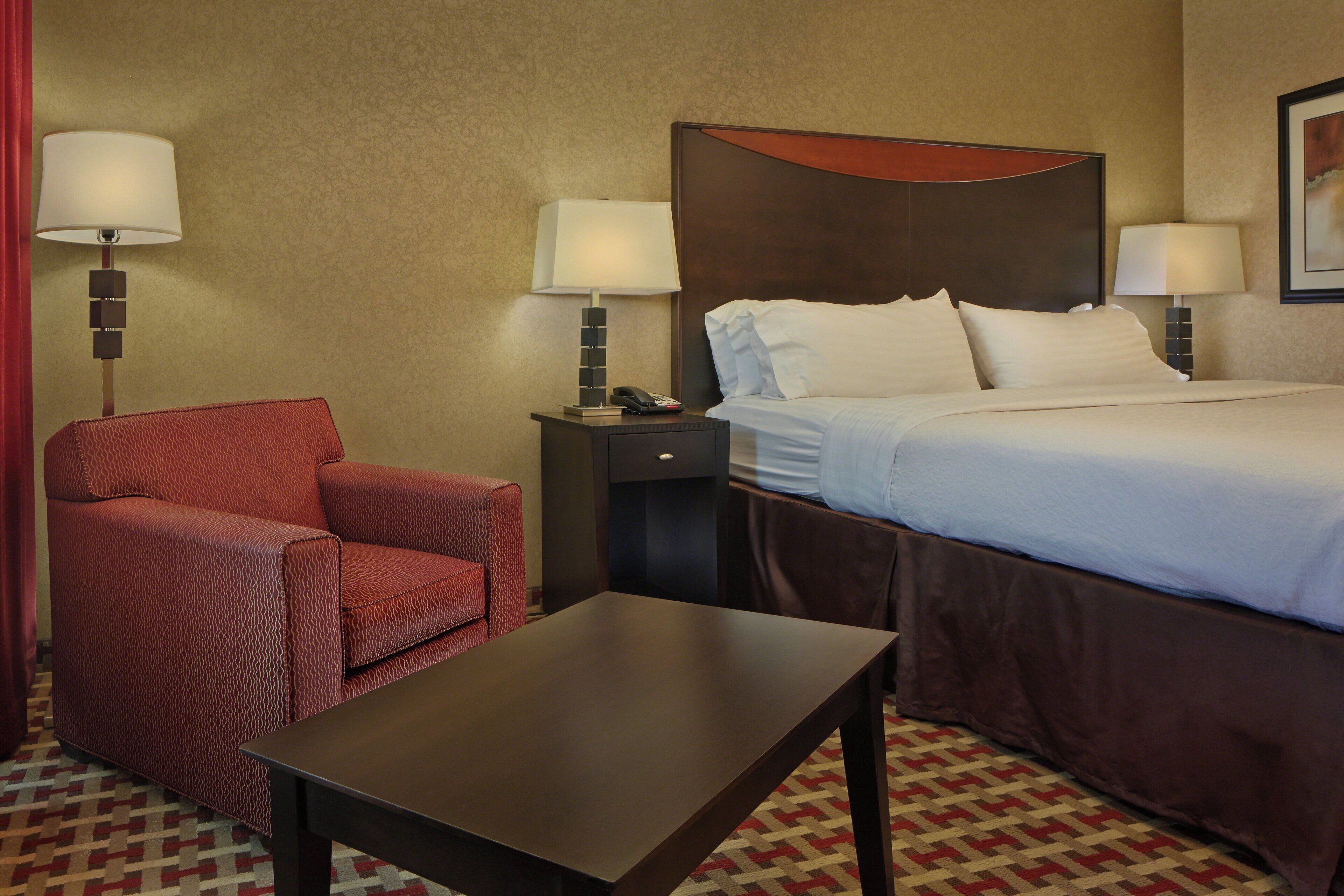 Una habitación de hotel con una cama, un escritorio, una silla y dos lámparas de noche.