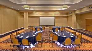 Un salón de conferencias con varias mesas y sillas, una pantalla de proyector y alfombra estampada.