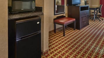 A compact hotel room with a refrigerator, microwave, television, and a small seating area.