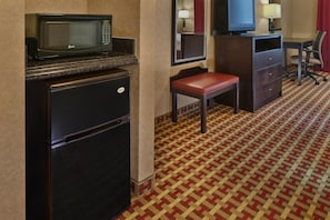 A compact hotel room with a refrigerator, microwave, television, and a small seating area.