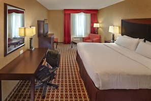 Une chambre d’hôtel avec un grand lit, un bureau avec une chaise, une télévision et un fauteuil rouge.