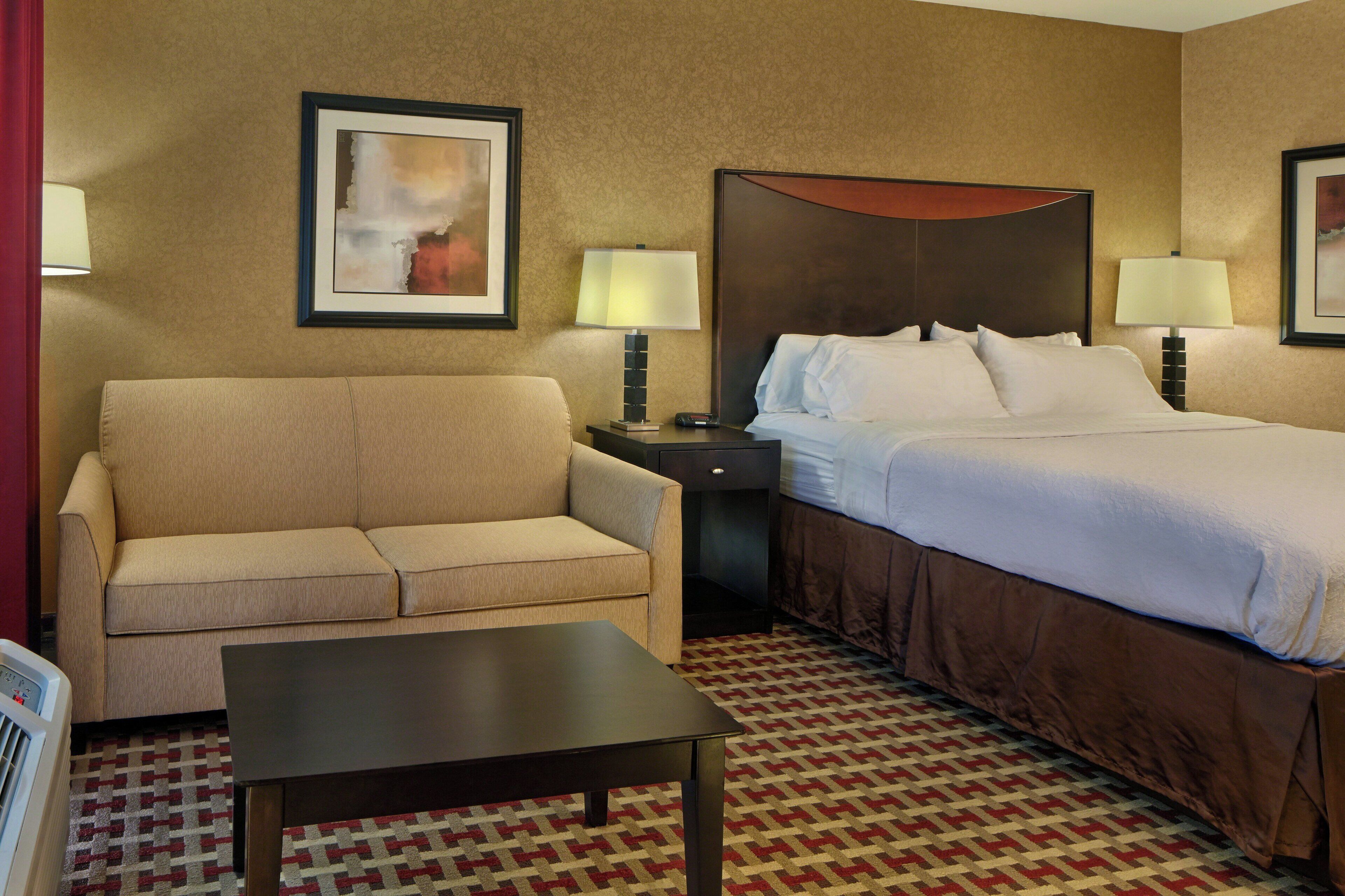 A hotel room with a bed, a sofa, a nightstand, two lamps, and a framed picture on the wall.