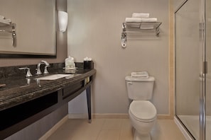 Une salle de bain moderne avec un plan de toilette en granit foncé, des toilettes blanches, une douche en verre et un porte-serviettes mural.