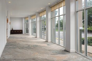 A corridor with large windows, a patterned carpet, and a wooden bench.