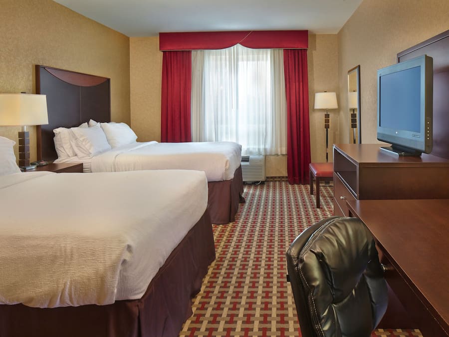 Habitación de hotel con dos camas, un escritorio, un televisor y una ventana con cortinas rojas.