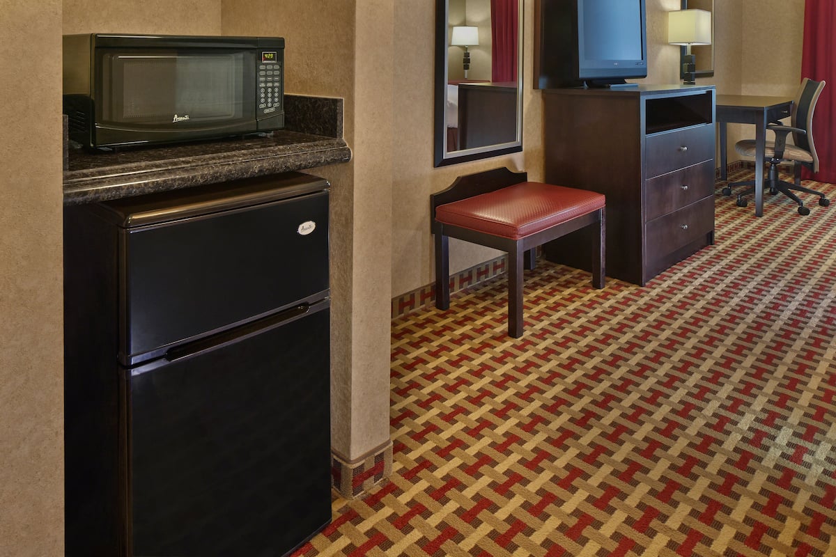 Une chambre d’hôtel compacte dotée d’une kitchenette, comprenant un four à micro-ondes, un réfrigérateur et un petit bureau avec une chaise.