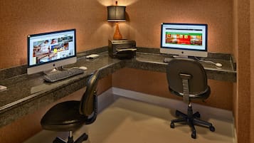 A workspace with two desktop computers, a lamp, a printer, a keyboard, and two office chairs.