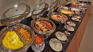 Un bufé con diversas opciones de comida, incluyendo papas, tocino y una variedad de frutas y verduras.