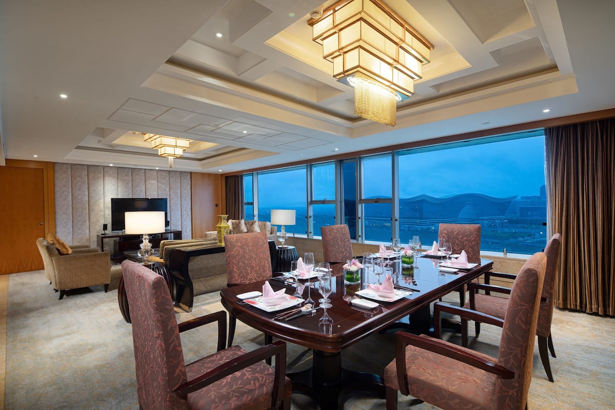 A hotel room with a dining area, a television, and a large window with a city view.